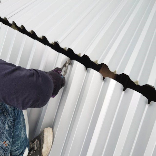 折板屋根の棟部分に折込みレイシャウトを行う職人